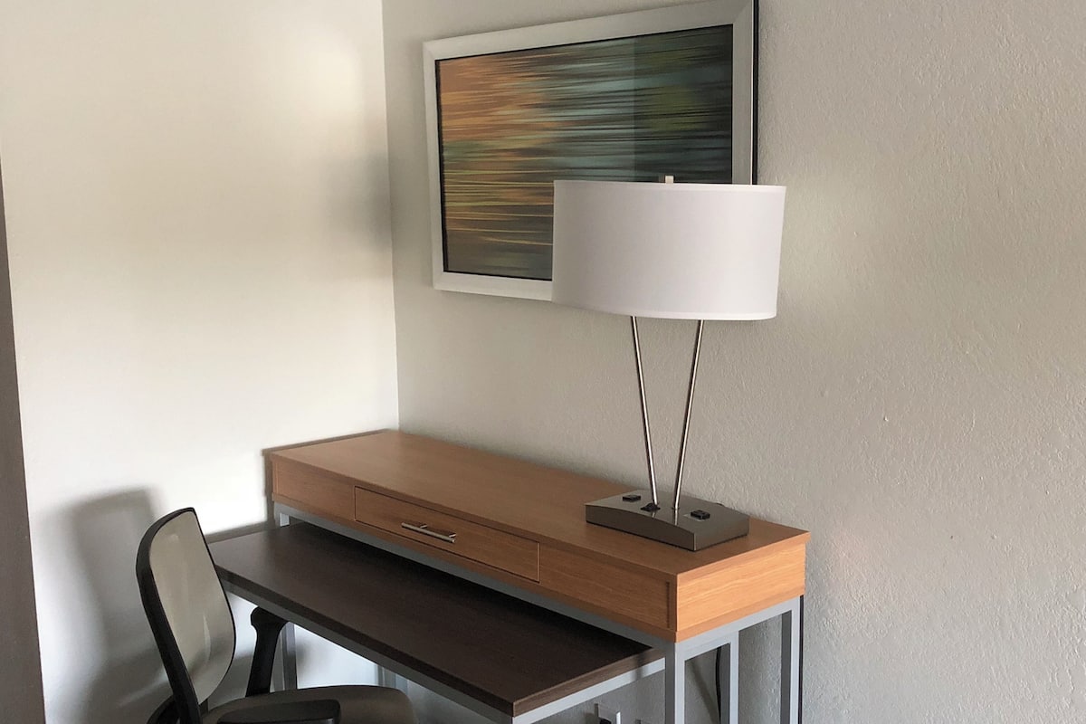 A desk with a lamp, a chair, and a painting on the wall.