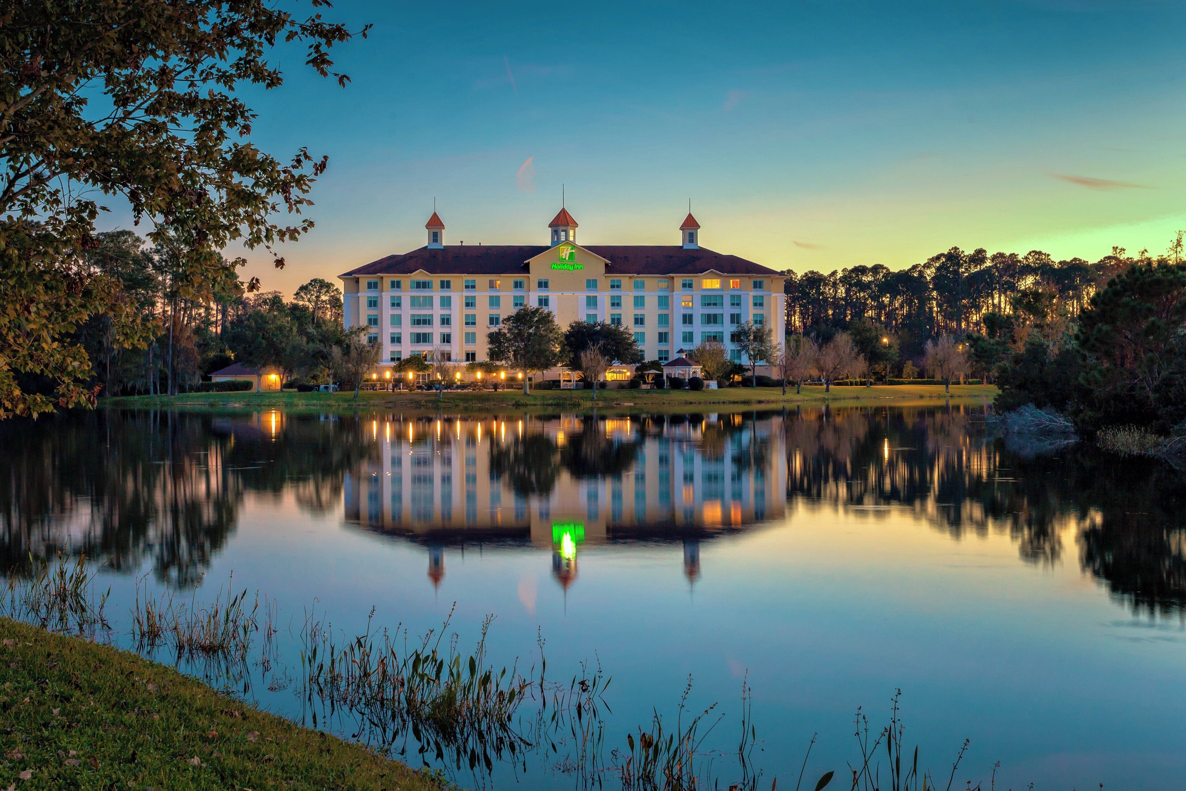 A large hotel with a symmetrical facade, a central tower, and a reflection in the water.