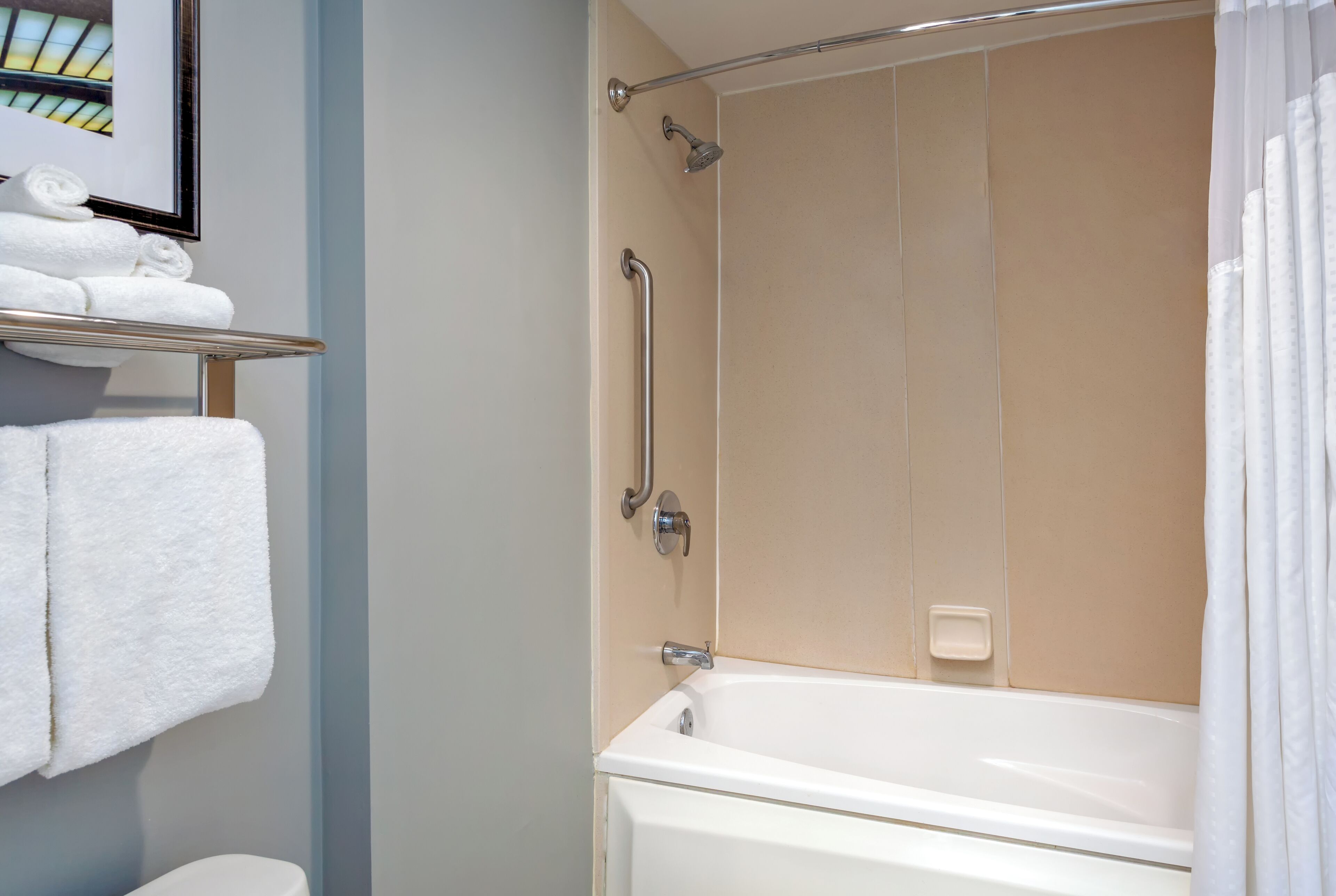 A bathroom with a bathtub, a shower with a grab bar, and a shelf with folded towels.