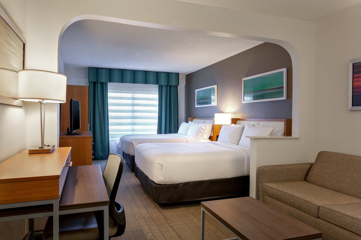 A hotel room with two beds, a desk, a chair, a sofa, and a TV.