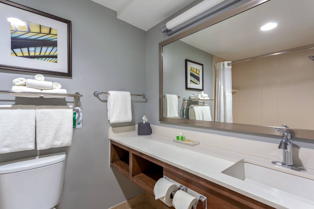 Une salle de bain moderne avec un grand miroir, un lavabo blanc et un porte-serviettes.