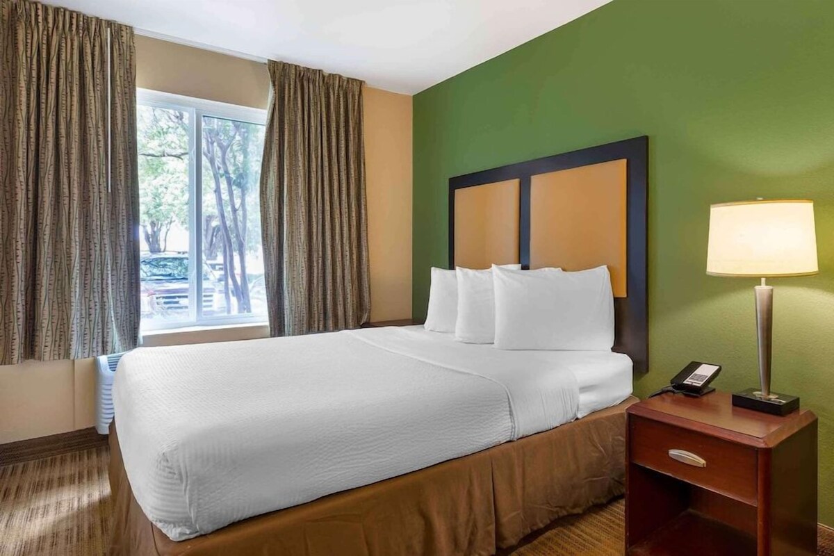 A hotel room with a large bed, a bedside table with a lamp, and a window with curtains.