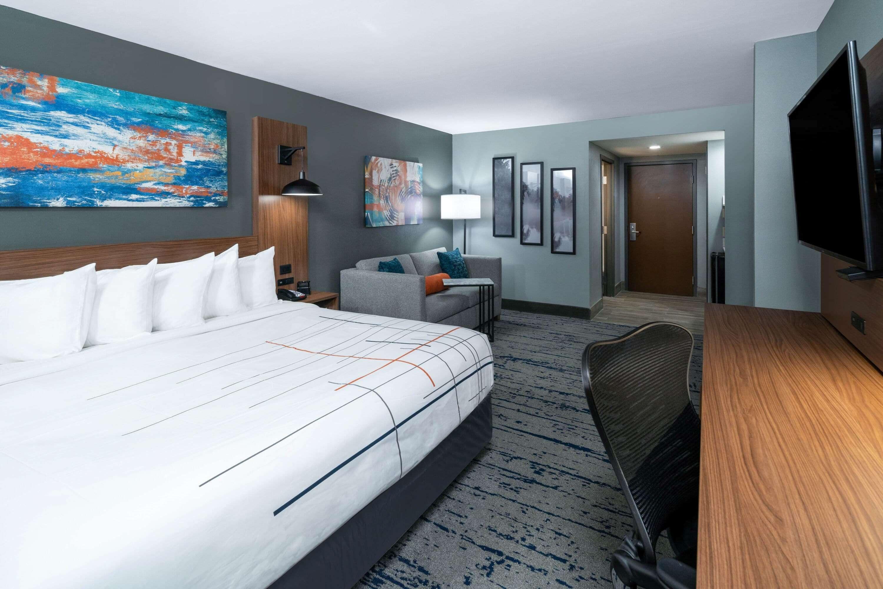 A hotel room with a large bed, a desk, a chair, a TV, and artwork on the walls.