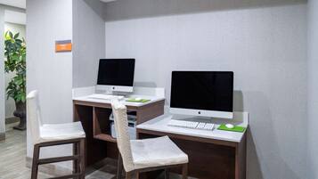 A workspace with two Apple iMac computers, two white cushioned chairs, a keyboard, a mouse, and a green mouse pad.