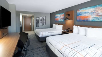 A hotel room with two beds, a desk, a chair, a TV, and artwork on the walls.