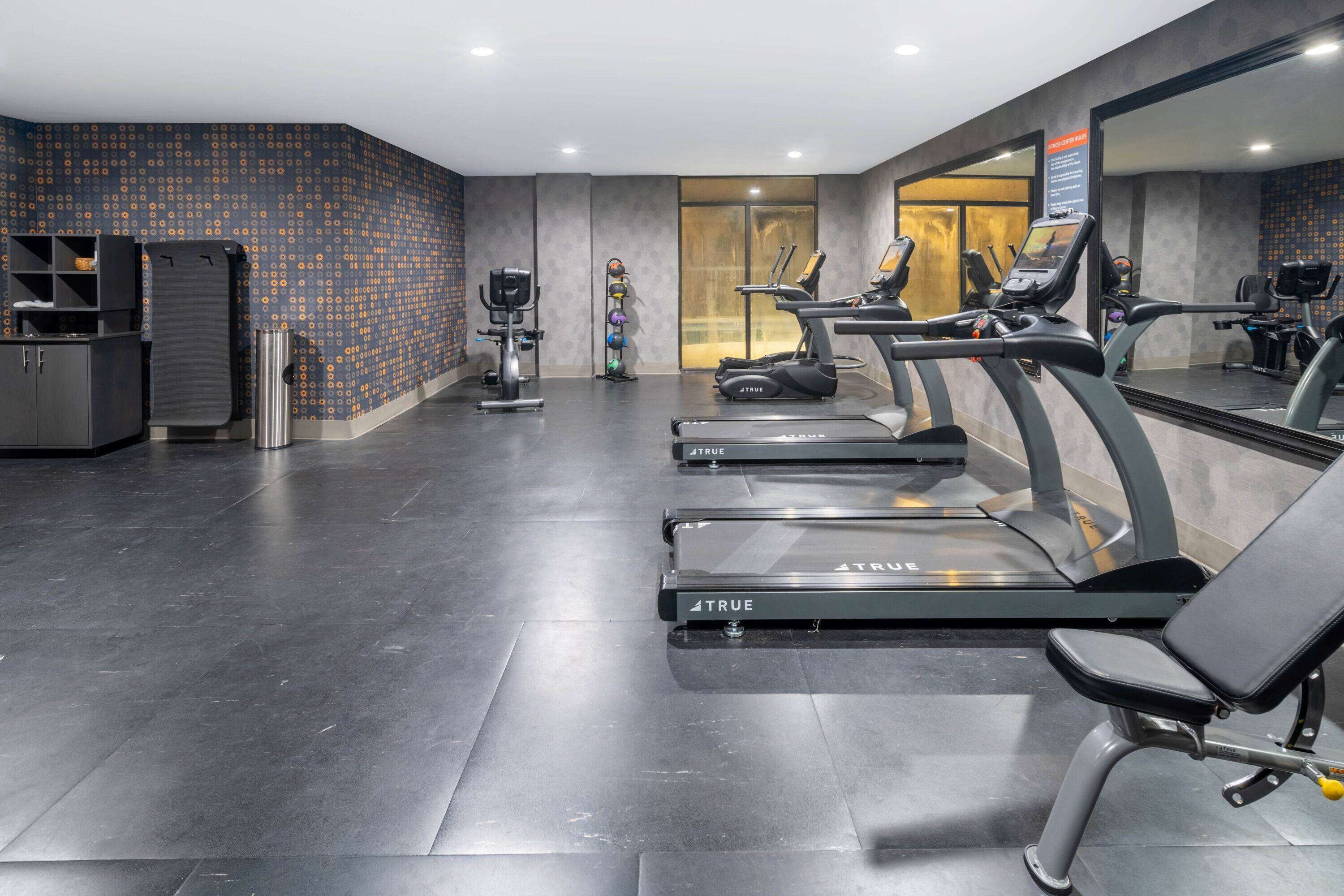 Una palestra con tapis roulant, cyclette e uno specchio a parete.
