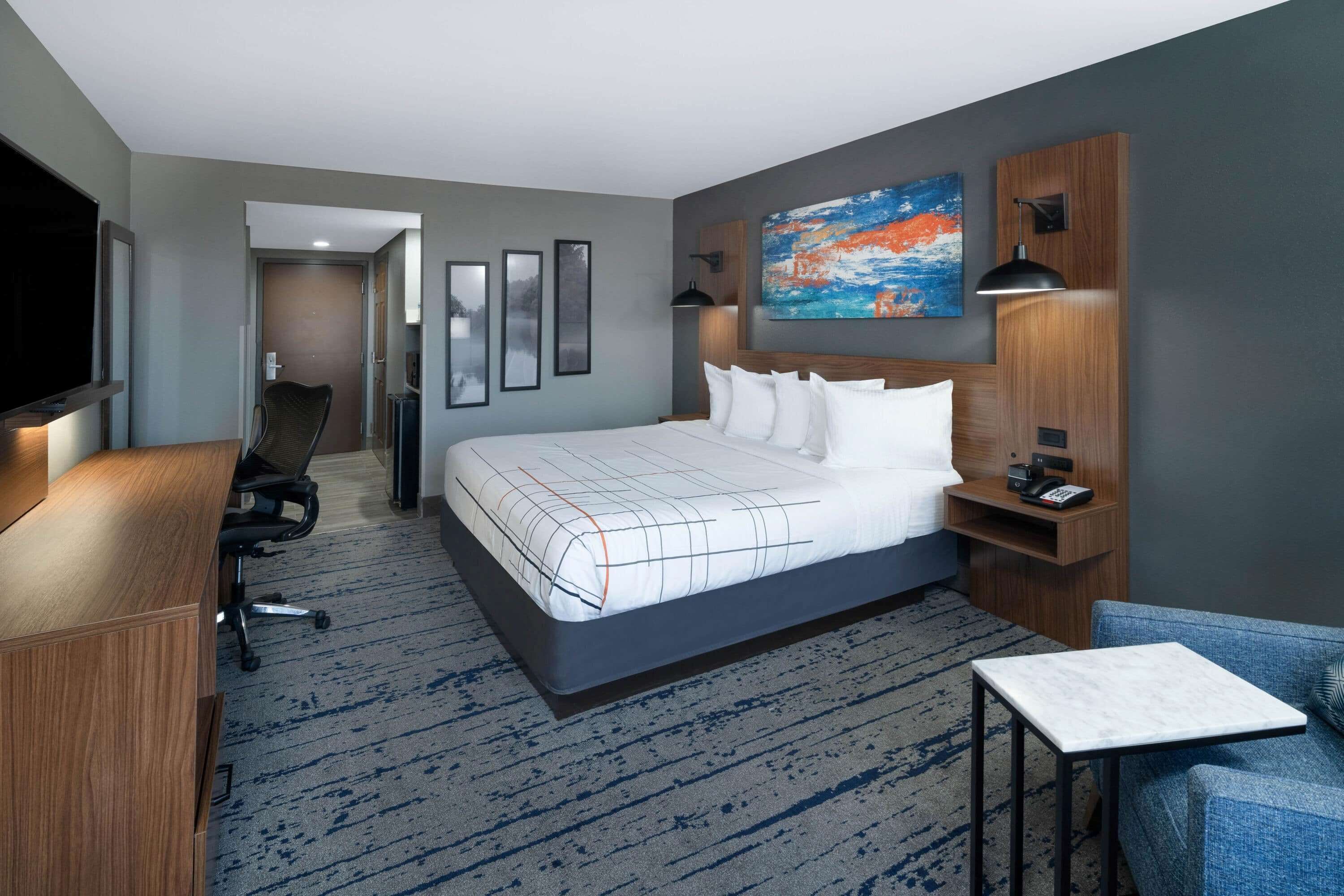 A hotel room with a large bed, a desk, a chair, a TV, and artwork on the walls.