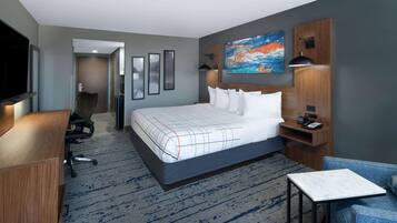 A hotel room with a large bed, a desk, a chair, a TV, and artwork on the walls.