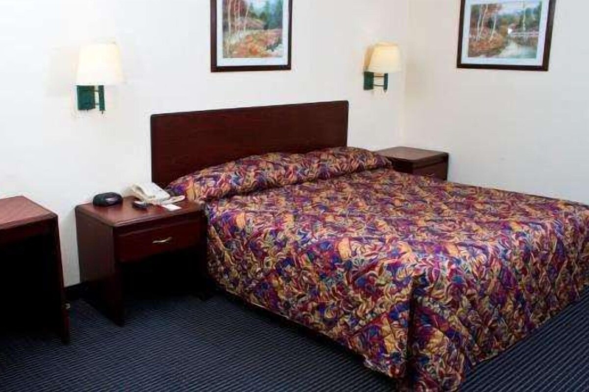 A hotel room with a bed, a desk, a chair, a nightstand, and two wall-mounted lamps.