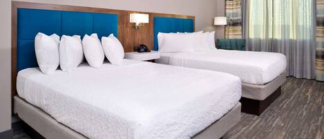 A hotel room with two beds, a wooden headboard, a nightstand, and a lamp.