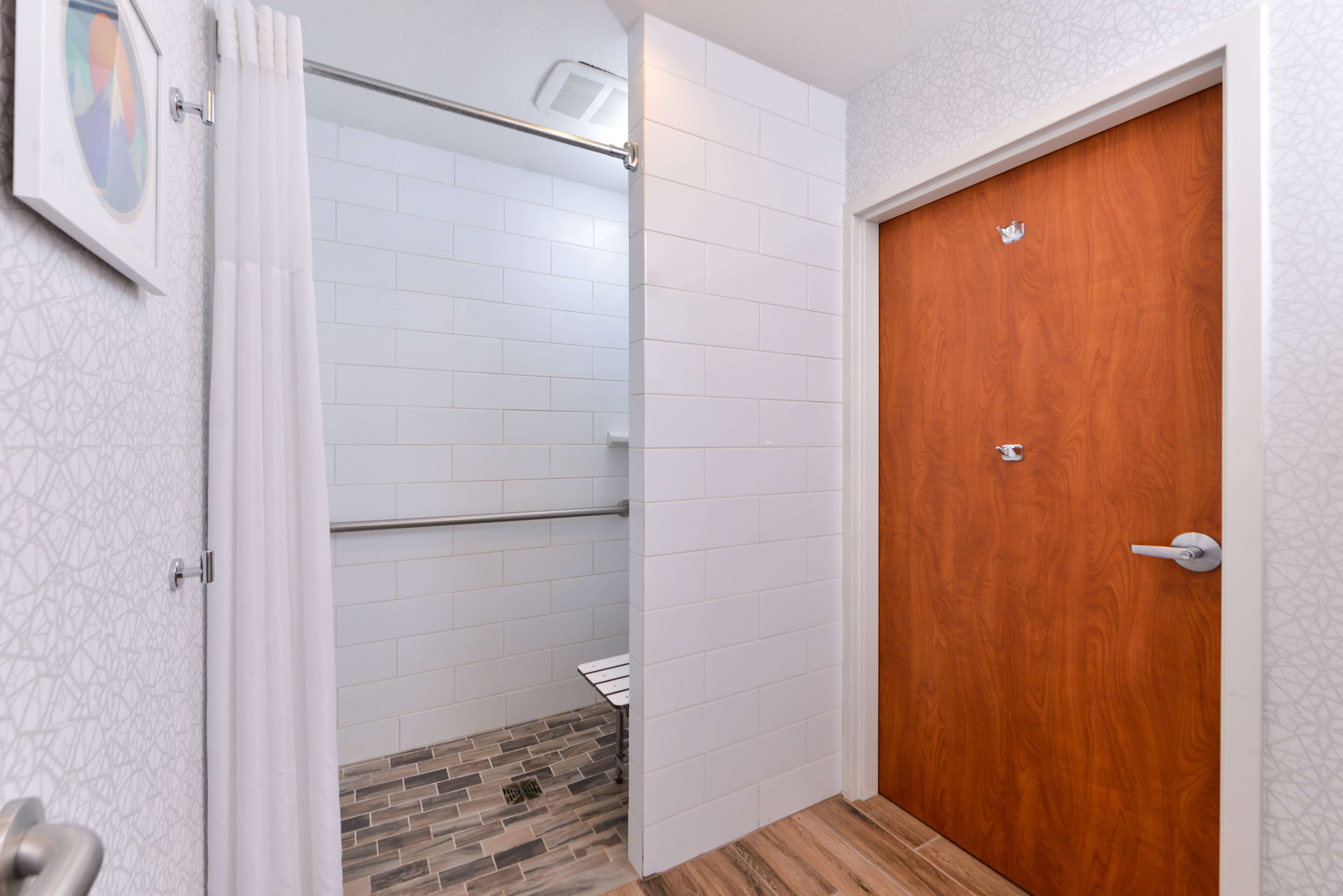 A bathroom with white tiled walls, a wooden door, and a shower area with a tiled floor.