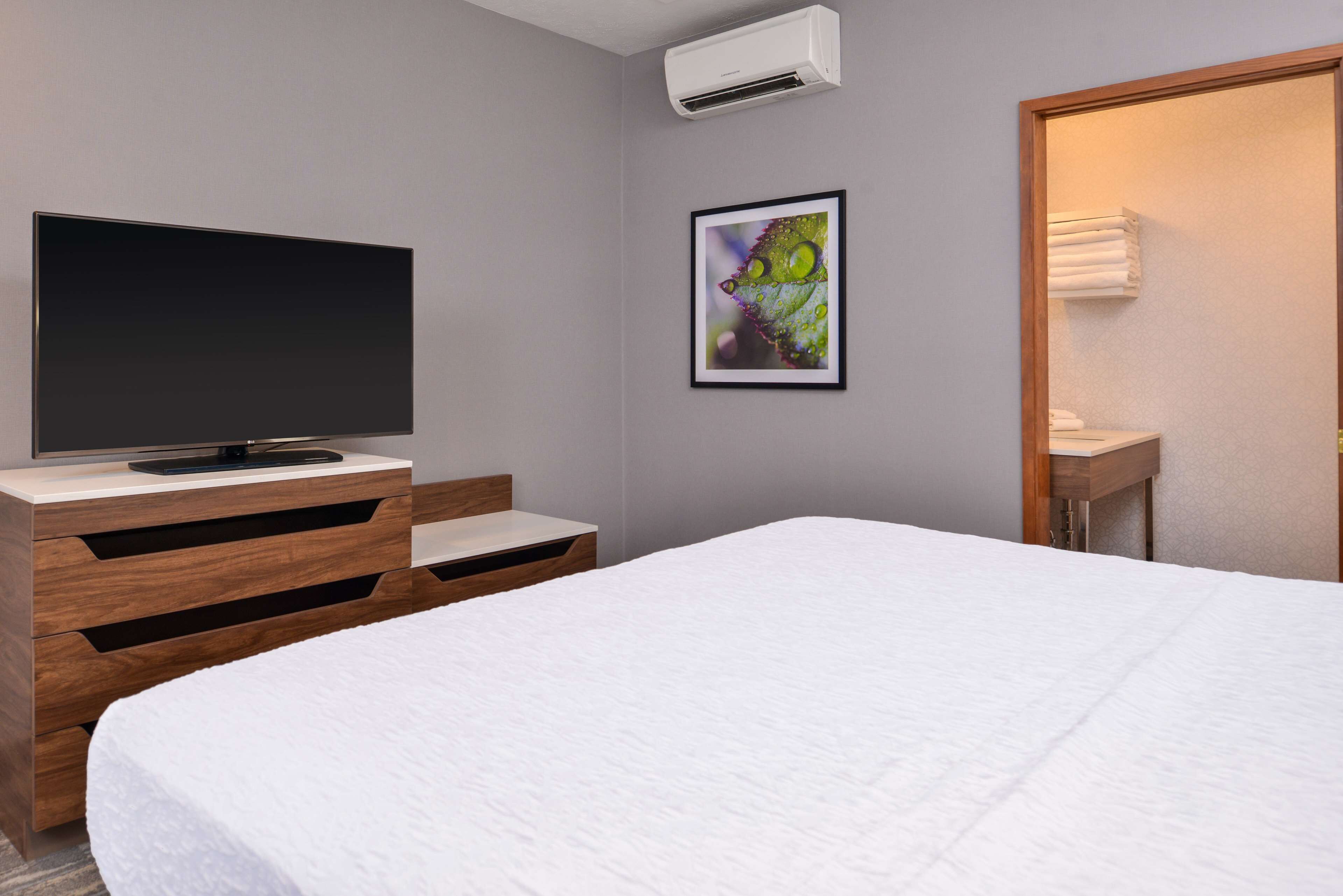 Een hotelkamer met een bed, een televisie op een houten dressoir, een lijst met een foto aan de muur en een badkamer met een handdoekhouder.