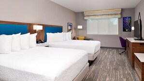 A hotel room with two beds, a desk, a chair, a TV, and a window with a view.