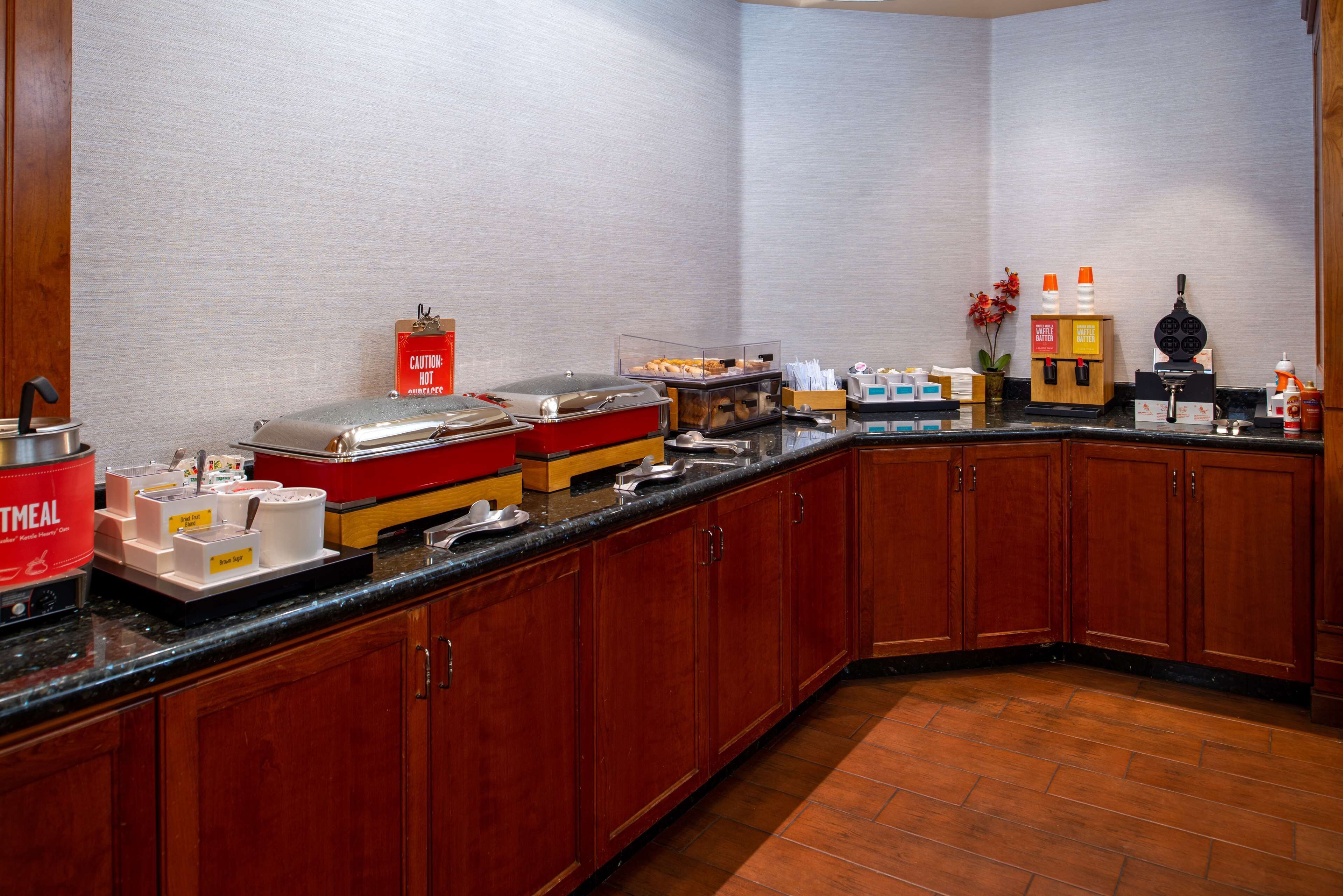 A hotel kitchen with a buffet setup, including various food containers and a caution sign.