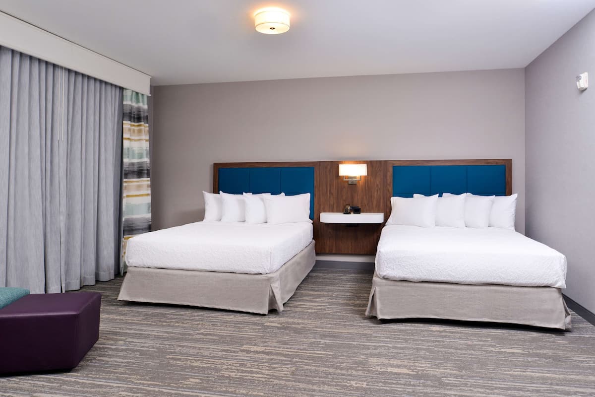 Habitación de hotel con dos camas, baño y un ventanal grande con cortinas.