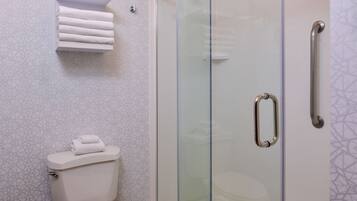 Un baño con cabina de ducha de vidrio, inodoro y toallero con toallas dobladas.
