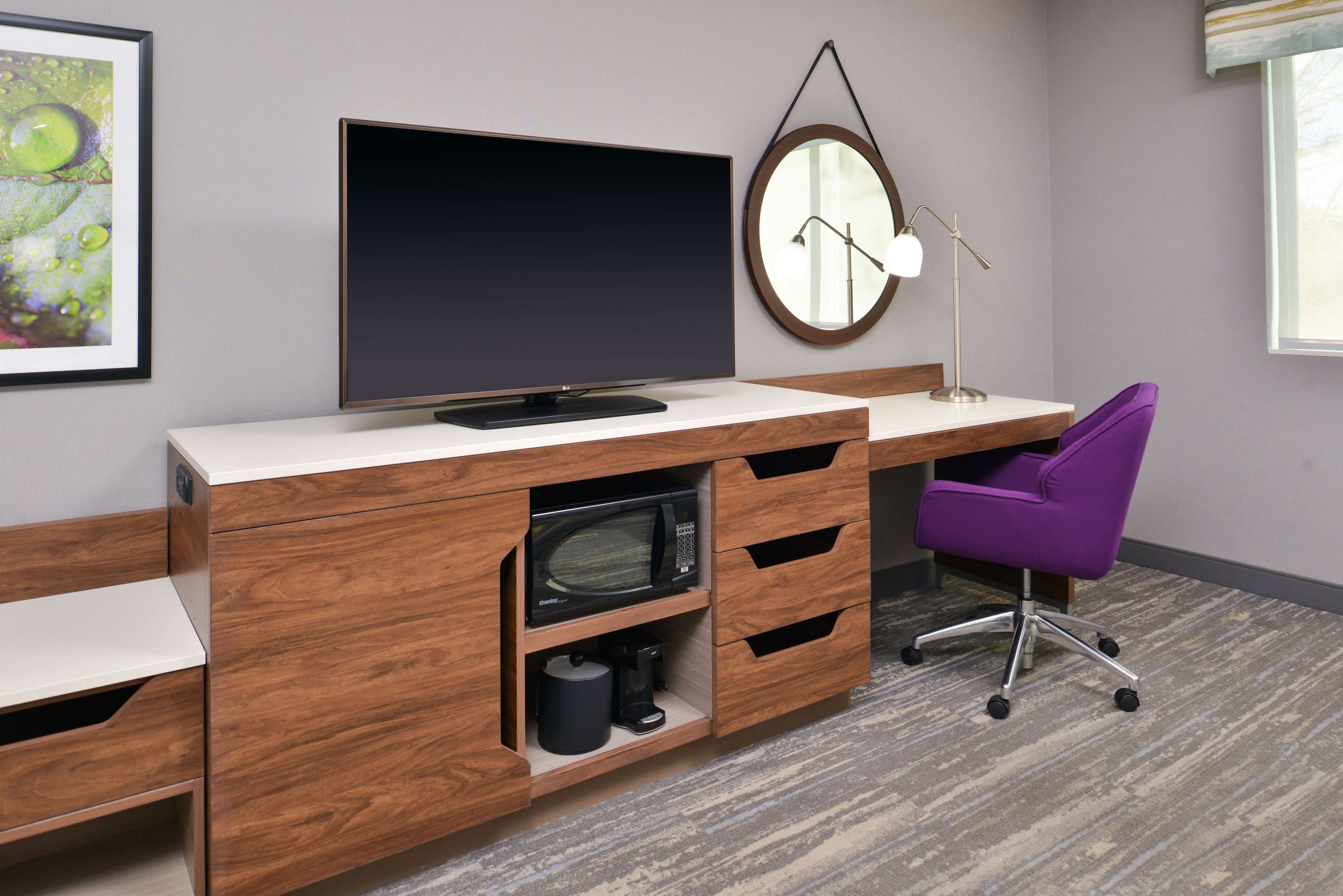 A modern office space with a wooden desk, a flat-screen TV, a round mirror, and a purple office chair.
