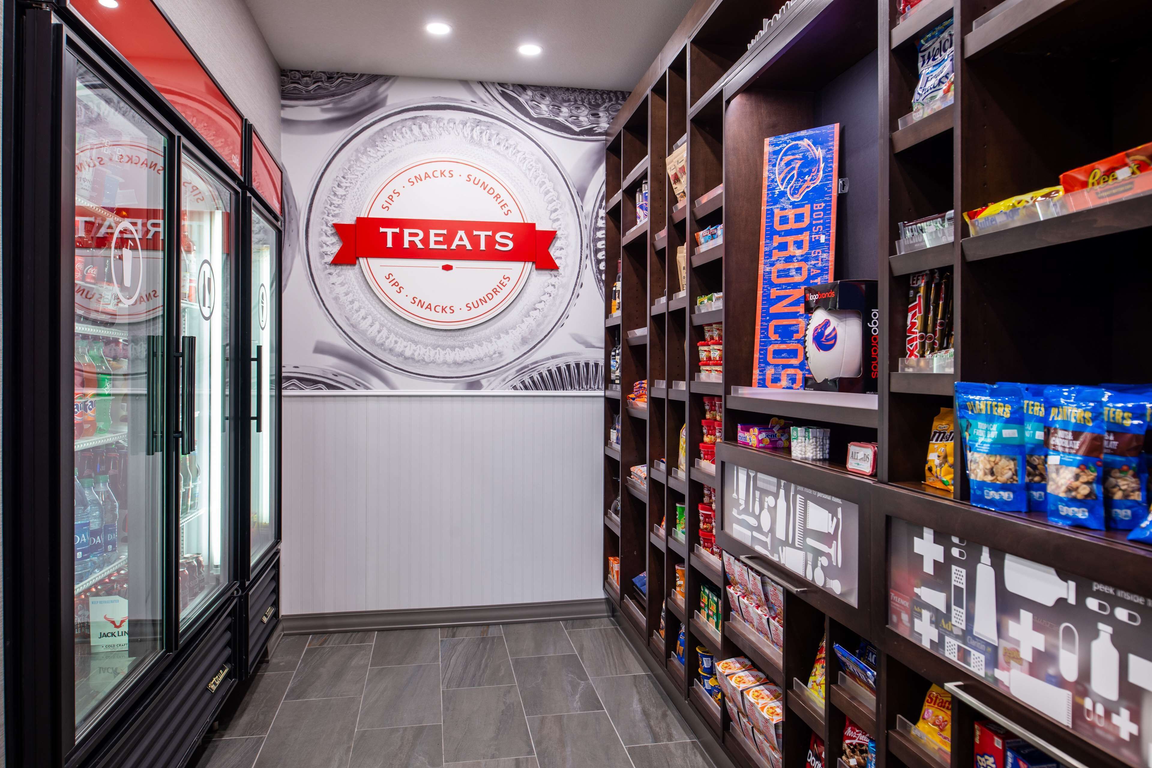 A corridor with shelves stocked with snacks and treats, a refrigerated display case, and a wall with a 'Treats' sign.