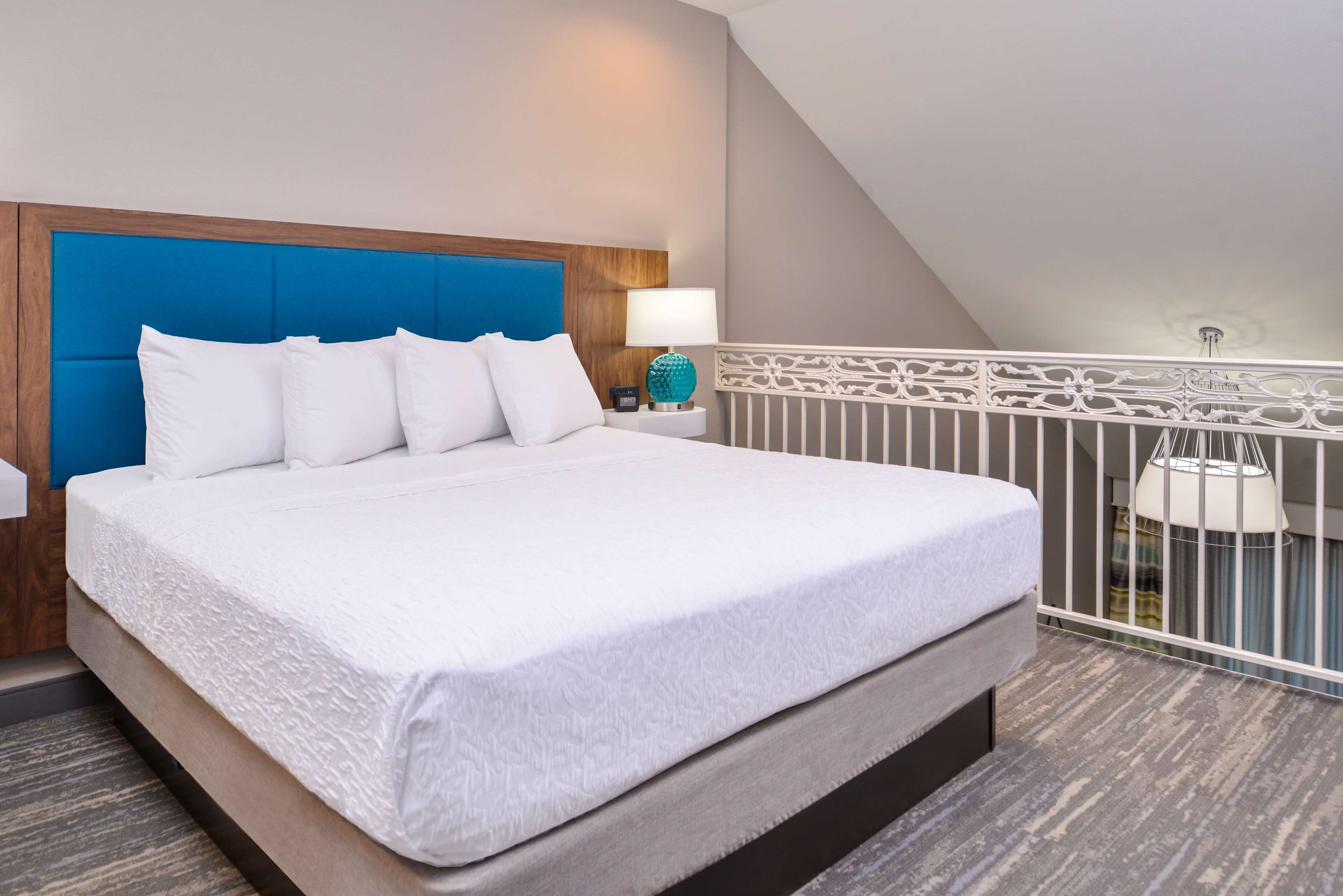 Ein Hotelzimmer mit einem großen Bett, einem hölzernen Kopfteil, einem Nachttisch mit Lampe und einem Balkon mit Geländer.