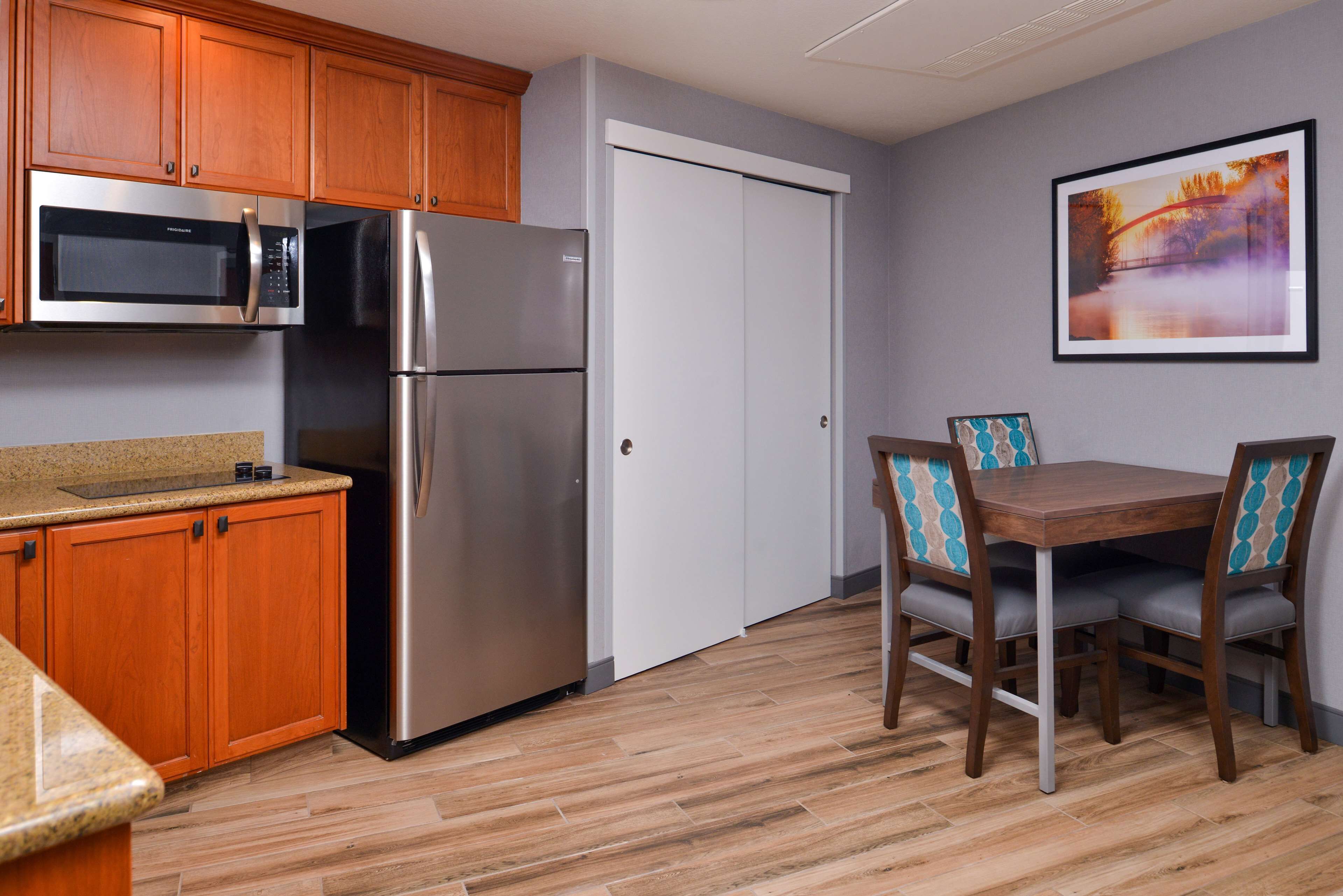 A kitchen with wooden cabinets, a stainless steel refrigerator, a microwave, and a dining table with chairs.