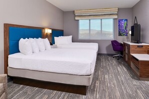 A hotel room with a large bed, a desk, a chair, a TV, and a window with a view of the mountains.