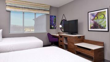 A hotel room with two beds, a desk, a chair, a television, and artwork on the walls.