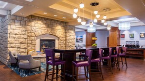 A bar area with stone walls, a fireplace, and purple bar stools. - Hampton Inn & Suites Boise/Spectrum (Boise)