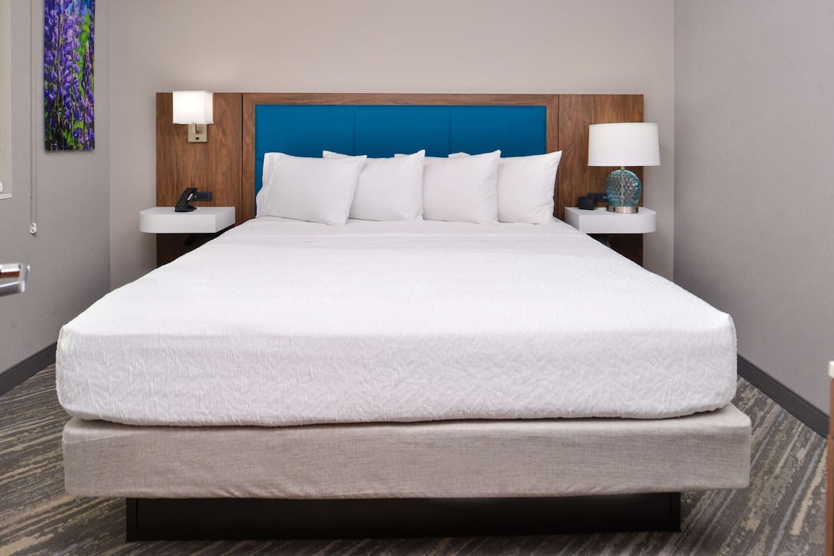 Una habitación de hotel con una cama grande, un cabecero de madera, dos mesitas de noche con lámparas y una lámpara fijada a la pared.