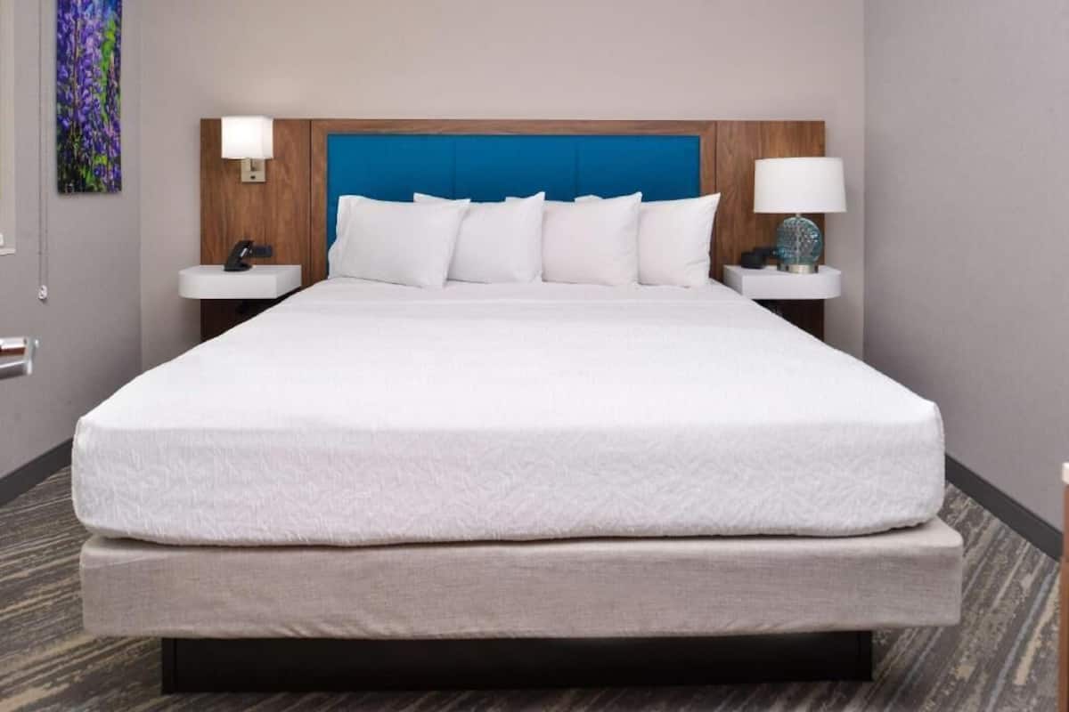 Una habitación de hotel con una cama grande, dos mesitas de noche, un cabecero y una lámpara de pared.