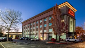 A multi-story hotel with a prominent sign, a parking lot with several cars, and a clear sky.