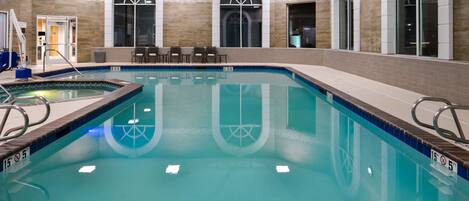 Uma piscina interior com água cristalina, bordas azulejadas e uma cadeira de salva-vidas.