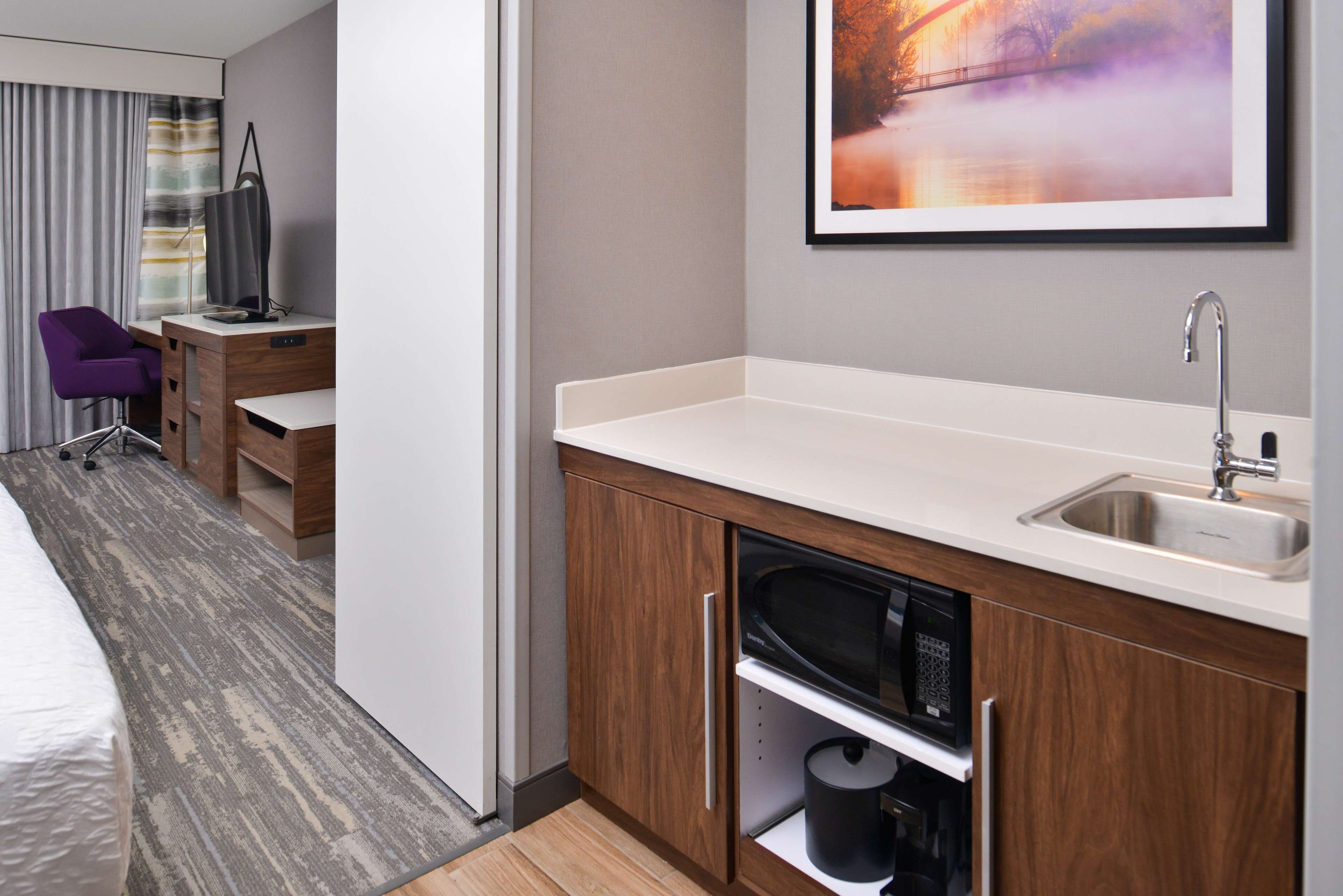 Una habitación de hotel moderna con kitchenette, una cama, un escritorio y una silla.