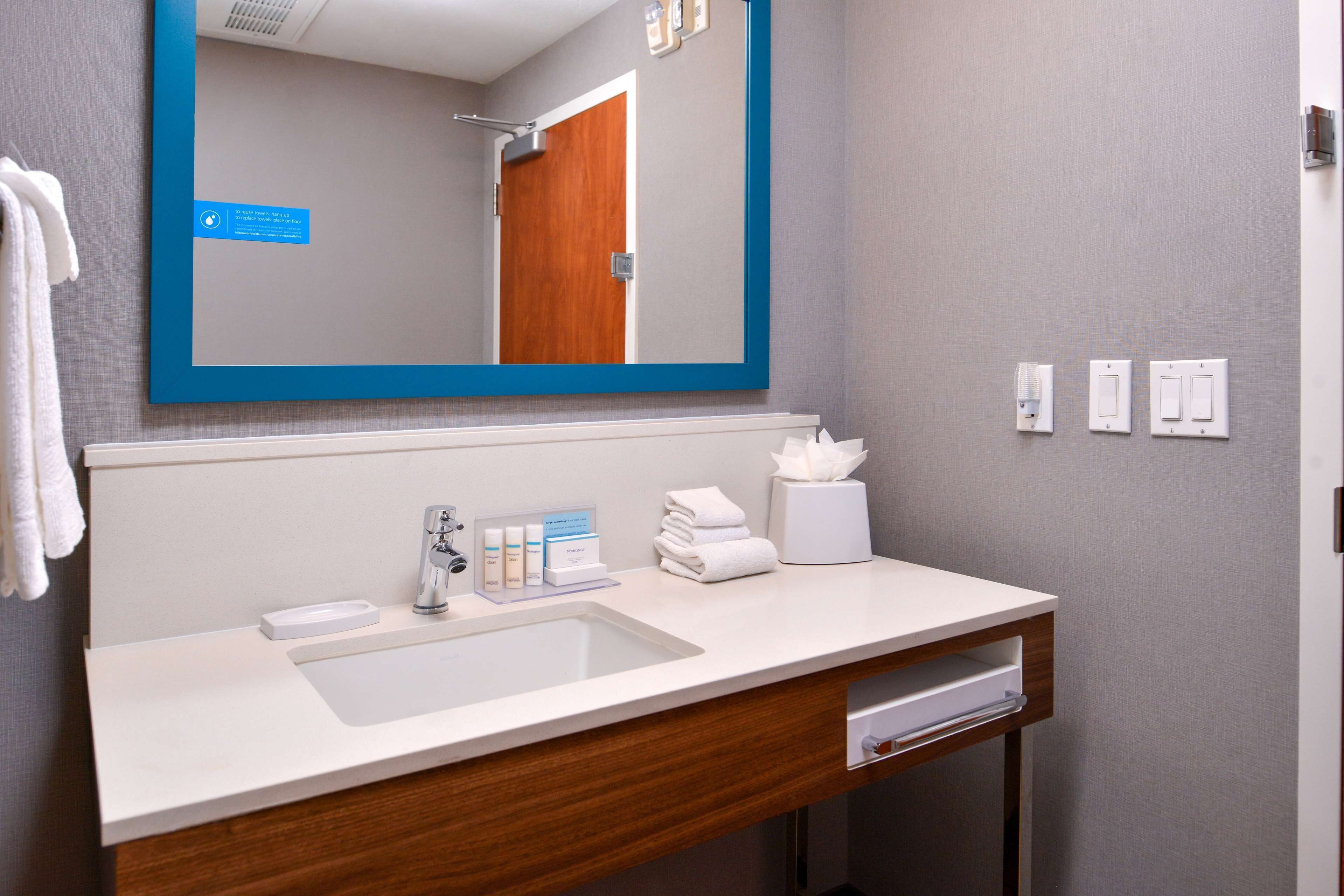 A modern bathroom with a large mirror, a sink, a towel dispenser, and a tissue box.
