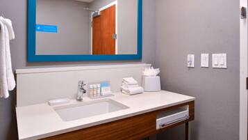 A modern bathroom with a large mirror, a sink, a towel dispenser, and a tissue box.