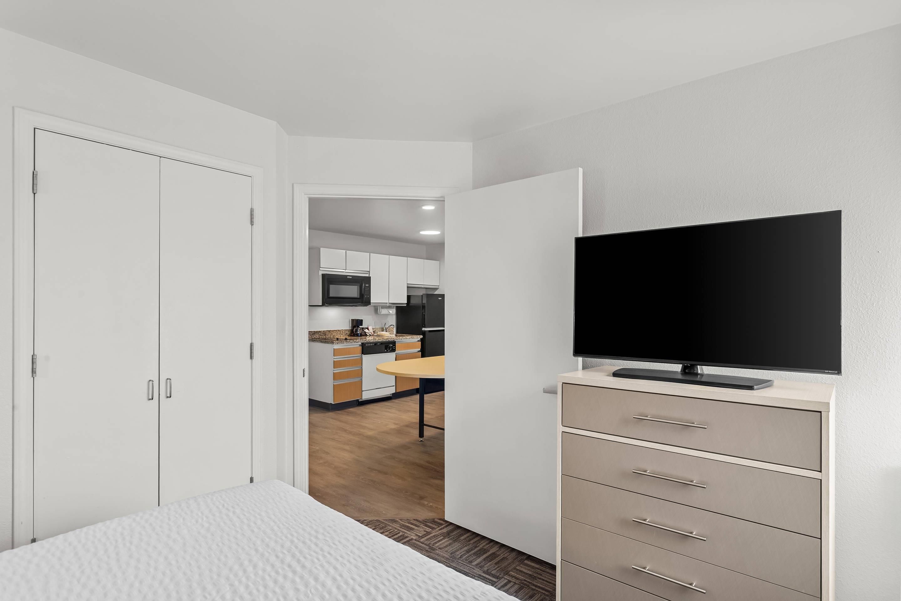 Ein Hotelzimmer mit einem Bett, einem Fernseher, einem Kleiderschrank und Blick zur Küche.