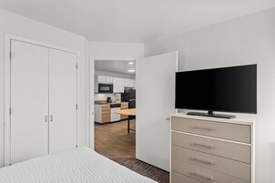 Una habitación de hotel con cama, televisor, armario y vista a la cocina.