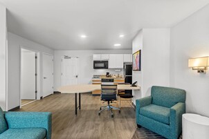 A modern apartment with a kitchen, dining area, and two teal armchairs.