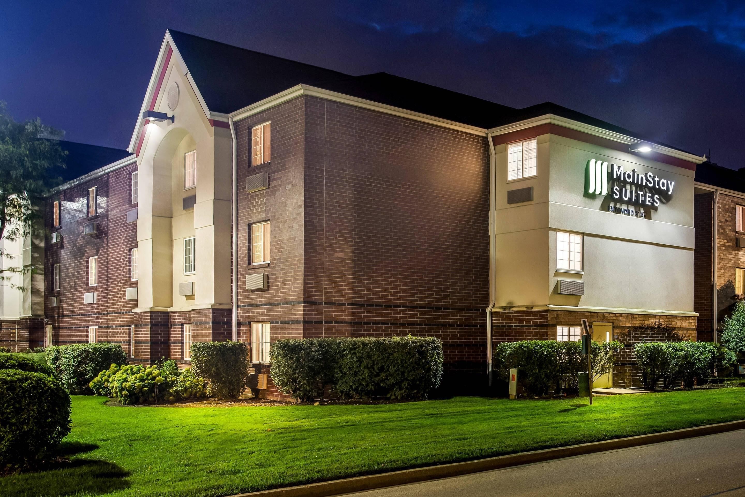 A MainStay Suites hotel with a brick facade, multiple windows, and a well-maintained lawn.
