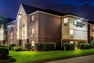 A MainStay Suites hotel with a brick facade, multiple windows, and a well-maintained lawn.