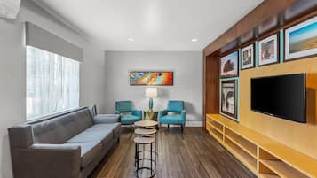 A modern living room with a grey sofa, teal armchairs, a coffee table, and a flat-screen TV mounted on a wooden wall.