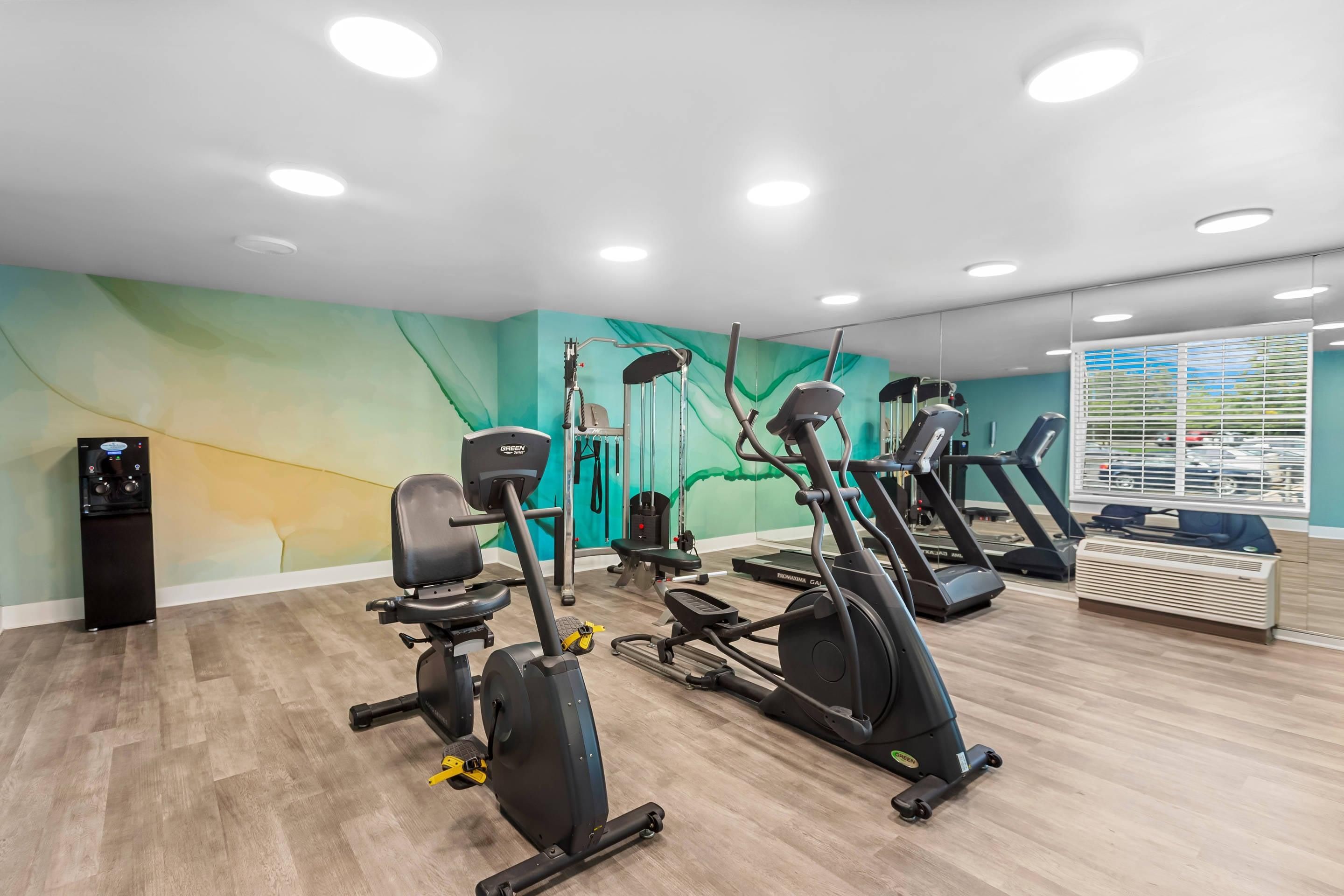 A gym with multiple exercise machines, a water dispenser, and a wall mural.