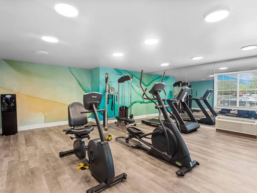 A gym with multiple exercise machines, a water dispenser, and a wall mural.