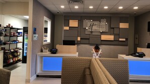 A hotel reception area with a modern design, including a reception desk, seating area, and a wall-mounted sign for Holiday Inn Express.