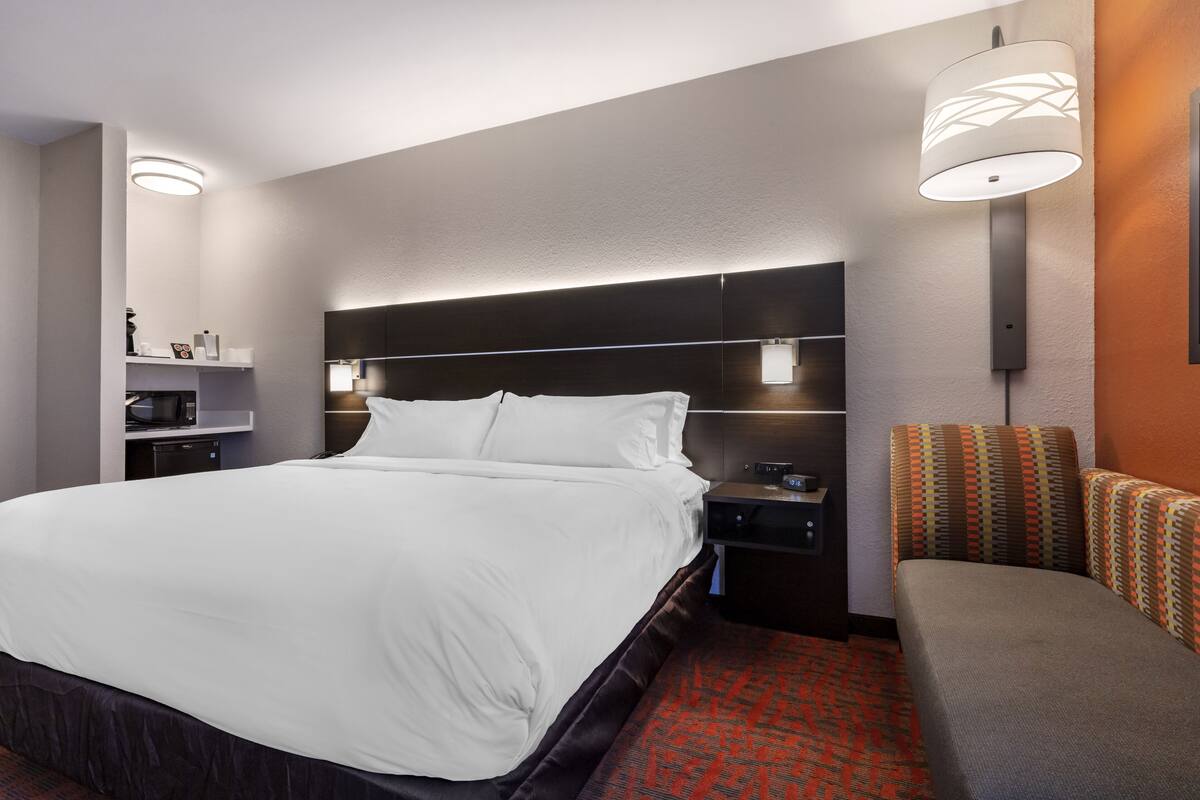 A hotel room with a large bed, bedside tables, a nightstand, a lamp, and a patterned armchair.