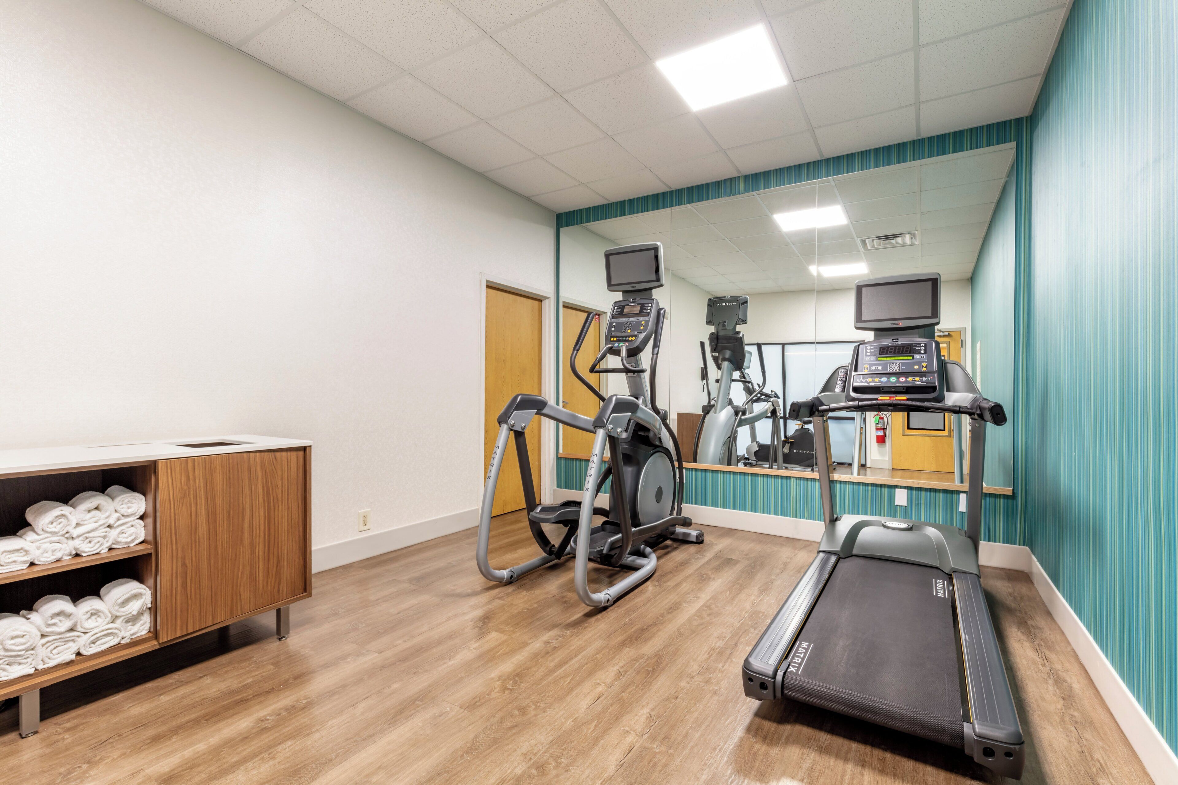 Gimnasio con equipamiento de ejercicio, un espejo y un armario de madera con toallas.