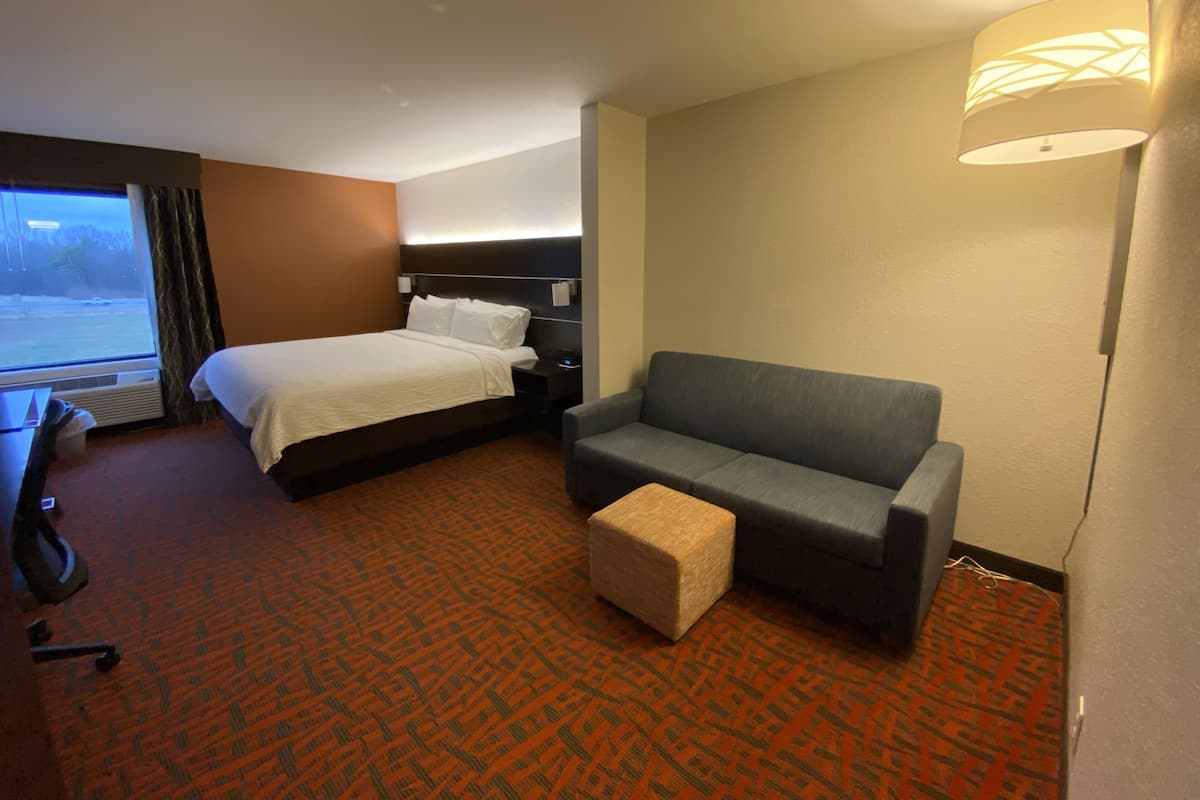 A hotel room with a bed, a sofa, a small ottoman, a desk, and a window with curtains.