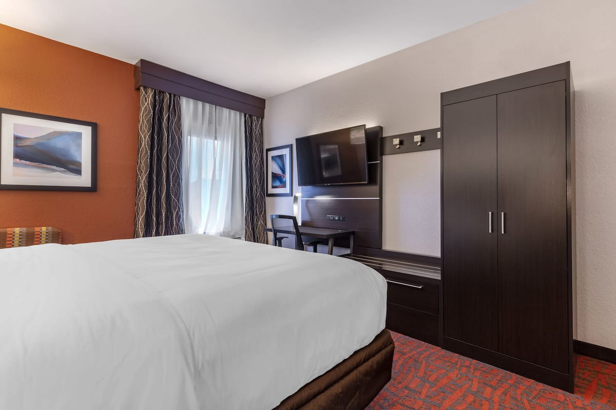 A hotel room with a large bed, a TV, a wardrobe, and a desk.