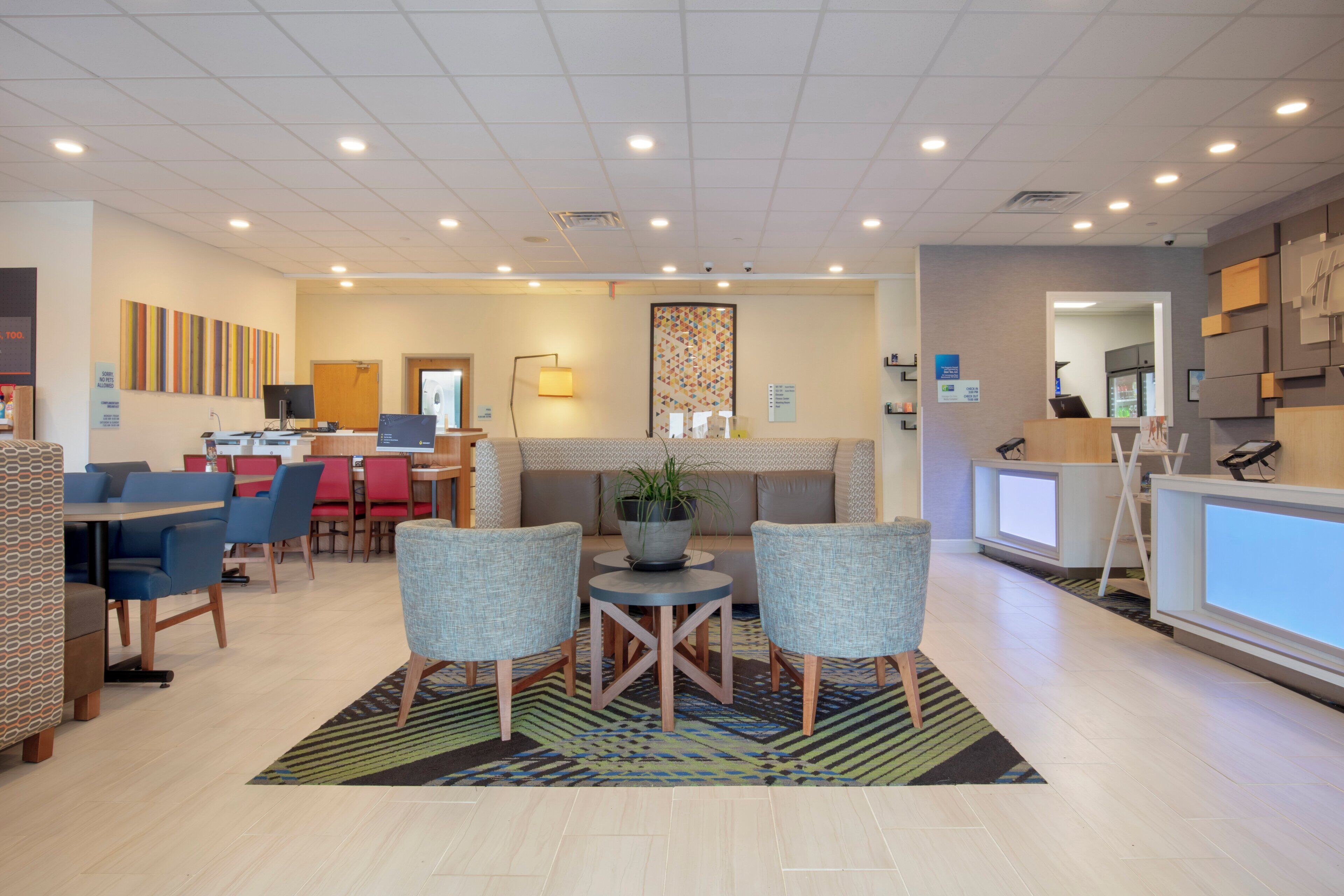 A modern hotel lobby with a reception desk, seating area, and a dining space.