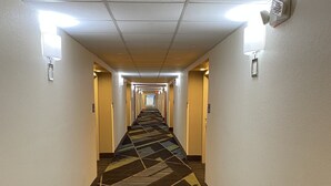 A hotel corridor with patterned carpet, wall-mounted lights, and doors on both sides.