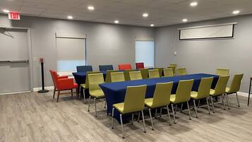A conference room with a long table, yellow and blue chairs, and a projector screen.
